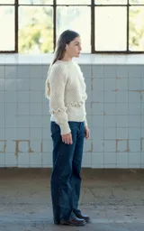 Sweater tejido a crochet en lana merino color crudo, con cuello redondo y manga larga. Presenta una trenza diagonal con volados en el frente.