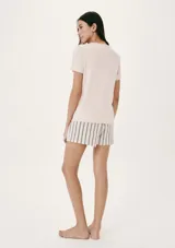 Pijama de dos piezas compuesto por una remera de manga corta color crema con un pequeño bordado de concha marina y un short de tiro alto con elástico y estampado de cuadrícula en tonos beige y blanco.