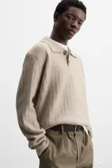Sweater color beige de punto canalé con cuello polo, solapas amplias y cierre frontal con dos botones.