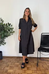 Vestido camisero largo color negro, de manga larga remangada, con cuello camisero y cierre frontal de botones. Corte amplio y falda con vuelo.