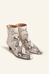 Botín blanco con estampado de piel de serpiente, punta fina y taco chupete. Cierre con cremallera en la parte trasera.