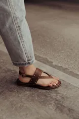 Sandalias marrones de cuero con tiras, microtachas doradas y hebilla lateral.