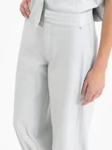 Pantalón de cuero ovino color gris claro, con frunces en el puño de la botamanga que aportan volumen. Tiene cintura doble con pespunte y botones forrados en cuero.