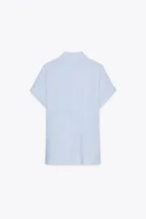 Camisa celeste de manga corta con cuello solapa y cierre frontal con botones. Tiene un nudo en la parte delantera.