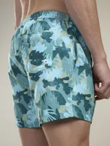 Short de baño verde con estampado de margaritas blancas y cordón ajustable naranja.