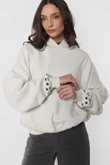 Buzo tipo hoodie color beige, de frisa gamuzada, con silueta oversize, bolsillo canguro, puños y cintura de ribb, capucha forrada con jersey y aplique de ojalillos en los puños.