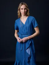 Vestido de tencel azul con escote en V cruzado, cintura elastizada con lazo, manga corta con volados y falda midi con volados.