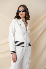 Chaqueta blanca de cuero ecológico, corte biker, con cierre frontal asimétrico y bolsillos con cierre. Detalle de puños elásticos con rayas horizontales negras.