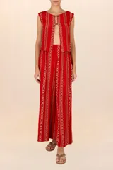 Chaleco rojo con estampado de cadenas doradas, sin mangas y con cuello redondo. Cierre frontal con ojales, botones dorados y cordones entrelazados.