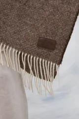 Ruana color crudo con rayas verticales finas en beige y flecos en el borde inferior.