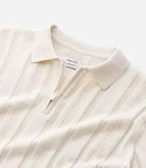 Camisa de punto color crema, con cuello polo y cierre frontal parcial con cremallera, de manga corta y diseño texturizado con perforaciones verticales.