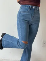 Pantalón de jean azul de tiro alto, corte semioxford y detalle de rotura en la rodilla.
