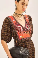 Vestido largo de viscosa con estampado geométrico en tonos marrón y naranja. Presenta escote en V con un panel bordado en la zona del busto en tonos naranja, rojo y blanco. Tiene mangas cortas abullonadas y cintura marcada con elástico.