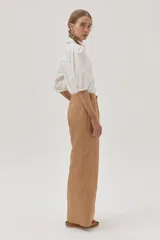 Camisa blanca de mangas abullonadas con puños elásticos, cuello clásico y cierre frontal con botones. Presenta detalles de bordado calado en el pecho.