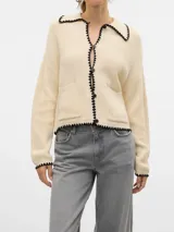 Cardigan tejido color crema con cuello polo, cierre con botones negros y ribete negro con forma de ondas en cuello, cierre, bolsillos y ruedo.