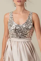 Vestido largo de fiesta color champagne, con corpiño de lentejuelas plateadas, falda de satén liso y lazo de satén en la cintura. Corsé de tul bordado. Talle único adaptable de S a L.