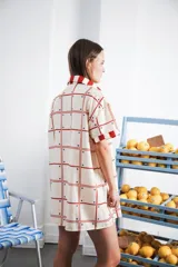 Vestido camisero corto con estampado a cuadros en tonos beige, rojo y azul. Tiene cuello camisero, botones frontales, bolsillo en el pecho y corte recto.