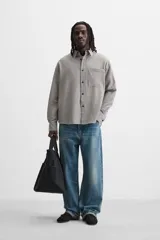 Camisa de hombre relaxed fit con cuello solapa, manga larga con puño abotonado, bolsillo de parche en el pecho y cierre frontal con botones. Diseño a cuadros en tonos gris y blanco.