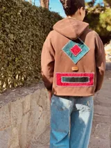 Canguro color chocolate de algodón con cierre parcial en el cuello y bolsillo frontal con apliques geométricos bordados a mano en terciopelo rojo y verde.