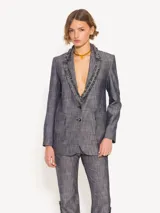 Blazer confeccionado en lino con apariencia denim, con solapa y cuello con flecos. Cierre con botones plateados y forro de tafeta jacquard.