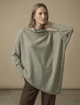 Poncho de tejido lurex color verde oliva con brillo sutil, de corte amplio y manga larga con puños acanalados. Presenta un bajo asimétrico con caída diagonal.
