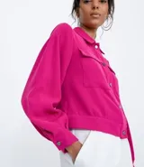 Campera color fucsia de crepe con cuello de camisa, manga abullonada, cierre frontal con botones y bolsillos frontales aplicados.