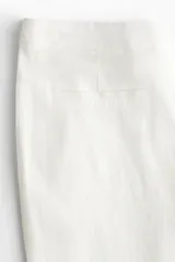 Pantalón sastrero de lino color blanco, de corte acampanado, tiro medio, cierre frontal con botón y bolsillos laterales.
