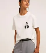 Blusa blanca de algodón con cuello redondo y mangas cortas. Presenta un estampado de una caricatura de una mujer con boina, lentes de sol y un trago en la mano.