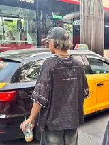 Camiseta negra con estampado de logos en gris y blanco, cuello redondo y mangas cortas. Diseño con ribetes blancos en cuello y mangas.