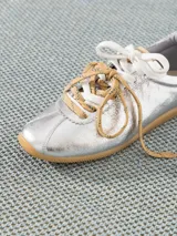 Zapatilla plateada de cuero vacuno con recortes en cuero descarne, doble cordón (uno blanco y otro marrón con pintitas) y charms colgantes.