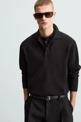 Polo de manga larga color negro, tejido en punto de algodón, corte relaxed fit, cuello solapa y cierre frontal con botonadura.