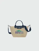 Bolso tote Longchamp modelo Le Pliage Collection S, color arena con detalles en azul marino. Presenta estampado frontal con el texto "Go the extra mile" y el logo de la marca. Incluye doble asa corta y correa larga extraíble.