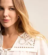 Blusa blanca amplia de viscosa, con lazo delantero, mangas largas abullonadas y canesú con encaje richelieu.