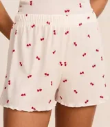 Conjunto de pijama short doll blanco con estampado de cerezas rojas, confeccionado en tejido rib. Incluye musculosa con puño y short con cintura elástica y bajo frufru.