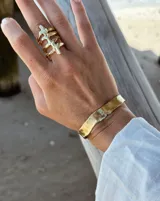 Pulsera tipo esclava abierta, con acabado rústico y textura irregular, en tono plateado. Se vende por unidad.