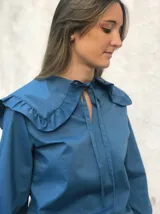 Blusa azul con cuello marinero con volados y lazos en el escote, mangas largas abullonadas con puños elásticos.