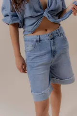 Bermuda de denim celeste, de tiro medio, corte relajado y largo por encima de la rodilla. Presenta doble ruedo con detalle desflecado.