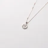 Colgante de plata con dije circular que enmarca dos corazones entrelazados. El borde exterior del dije está engastado con circones brillantes.
