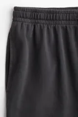Pantalón deportivo negro de corte holgado, con cintura elástica y cordón ajustable. Confeccionado en felpa de algodón liviano con efecto lavado, bolsillos laterales y bajos sin rematar.