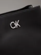 Cartera tipo saco Calvin Klein color negro, con correa ajustable para el hombro, compartimento central con cremallera, compartimento con cierre giratorio en la parte delantera, compartimento magnético en la parte trasera y herrajes plateados con el monograma de la marca.