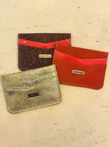 Tarjetero azul de cuero charol con tres ranuras para tarjetas y logo de la marca grabado en una placa dorada.