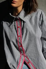 Camisa de poplin negro rayado con corte cómodo, mangas 3/4 y detalles ondeados al frente con zigzag de algodón fucsia y botones fucsia.