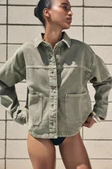 Cazadora de denim verde oliva, con cuello solapa, manga larga, bolsillos delanteros de plastrón y cierre frontal con botones metálicos.