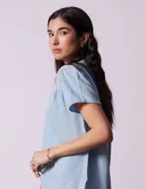 Camisa celeste de tencel con cuello con solapa, escote en V y abertura central con botones. Delantera con detalle en punto smock.