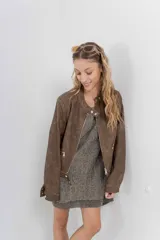 Chaqueta tipo biker de cuero ecológico (PU) color marrón con acabado desgastado, cuello Mao con broches metálicos, cierre frontal y bolsillos con cremallera.