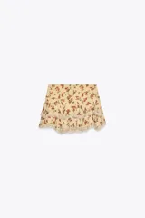 Minifalda color crema con estampado floral en tonos rojos y verdes. Presenta volados con puntilla en el ruedo.