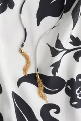 Vestido largo de corte holgado con estampado floral en blanco y negro. Tiene escote cuadrado con cordón ajustable y mangas cortas abullonadas con elástico en los puños. Presenta costura fruncida bajo la cadera.