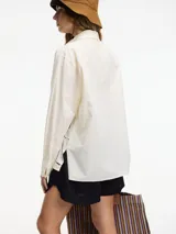 Camisa color crema con bordados y calados en el frente y la espalda, cuello camisero, botones frontales y mangas largas con puños abotonados.