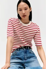Remera entallada de punto a rayas rojas y blancas con cuello redondo y mangas cortas con botones dorados en los hombros.