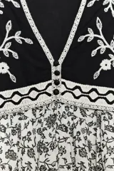 Vestido corto con estampado floral en blanco y negro, escote pico, mangas cortas abullonadas y detalle de chaleco negro con bordados y falsos botones delanteros. Incluye forro interior.